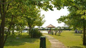 A park with a wooden pathway, a gazebo, and a pool area. - Cozy villa in a quiet area surrounded by nature of Lignano (Ente di decentramento regionale di Udine)