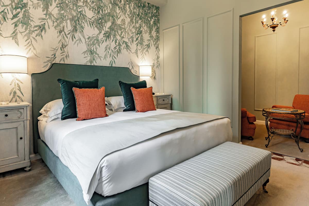 A neatly arranged bedroom with a large bed, two bedside tables, a chair, and a small table with a lamp.