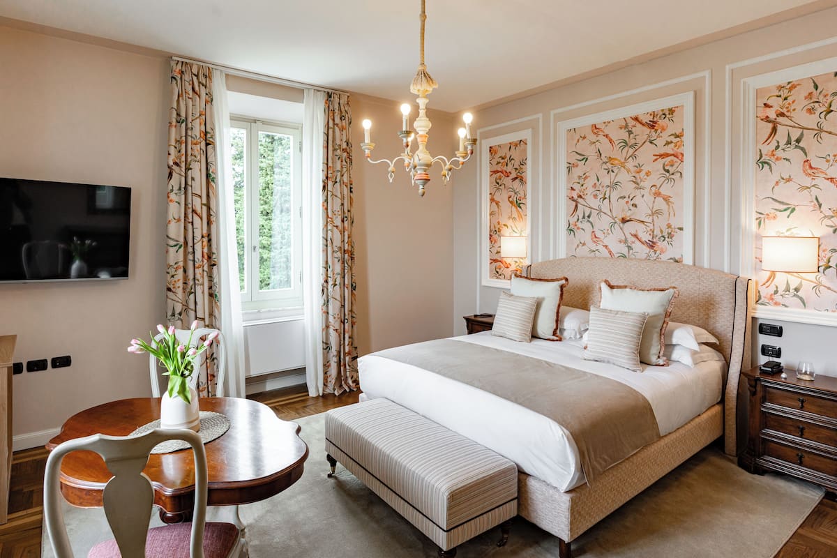 A bedroom with a large bed, a chandelier, a TV, and floral wallpaper.