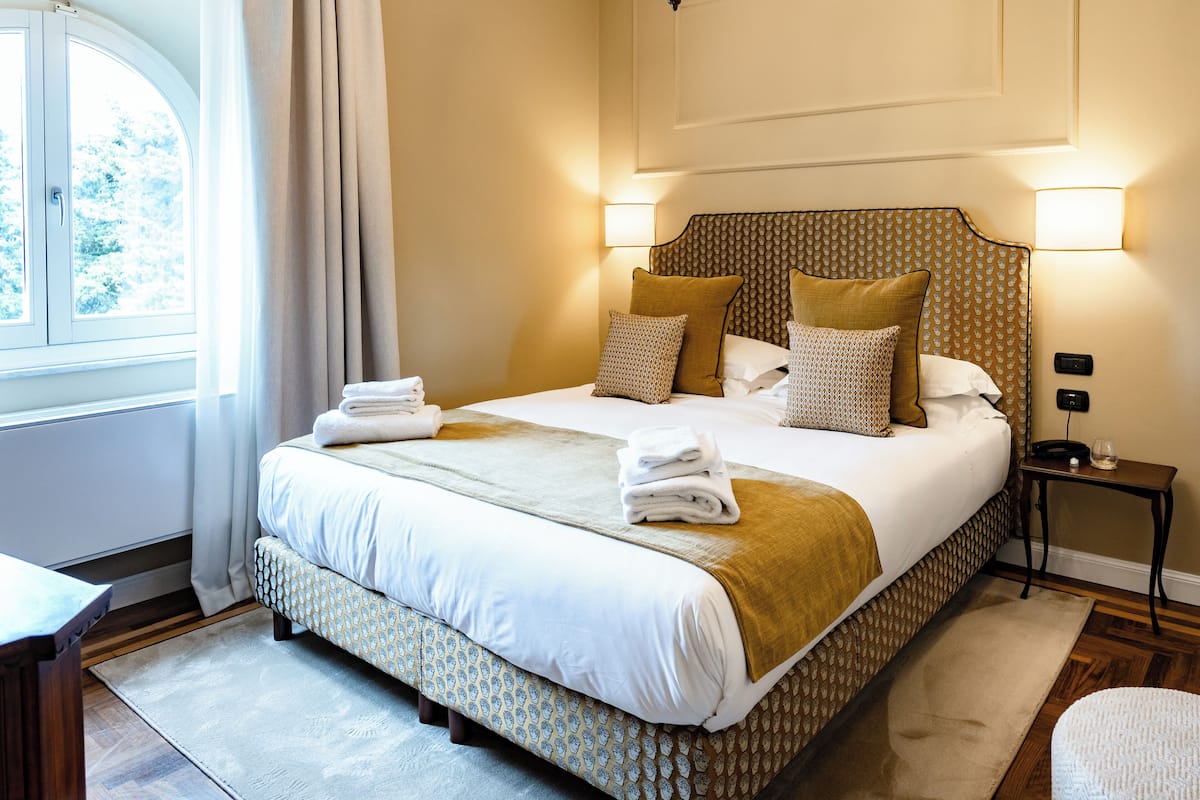 A neatly made bed with a patterned headboard, a bedside table with a lamp, and a window with curtains.
