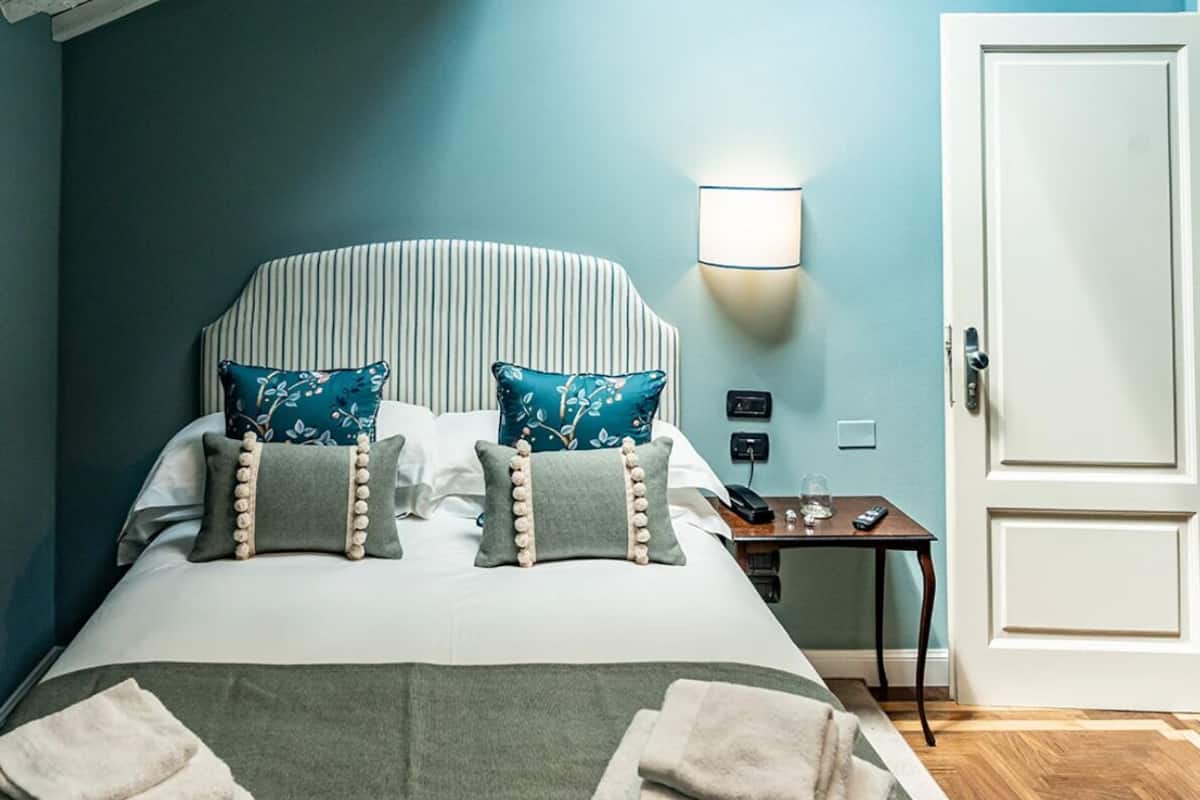 A neatly arranged bedroom with a large bed, two pillows, a bedside table with a lamp, and a door.