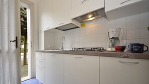 A kitchen with white cabinets, a gas stove, a coffee maker, and a coffee cup. - Stylish apartment with pool access (Bibione)