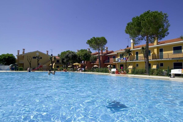 A swimming pool with people around it, surrounded by buildings with balconies and trees.