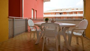 Een balkon met een ronde tafel en vier stoelen, een bloempot en uitzicht op een gebouw met balkons.