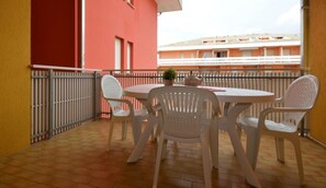 Een balkon met een ronde tafel en vier stoelen, een bloempot en uitzicht op een gebouw met balkons.