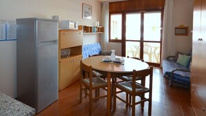 Een kleine keuken met een koelkast, houten kastjes en een eettafel met stoelen.