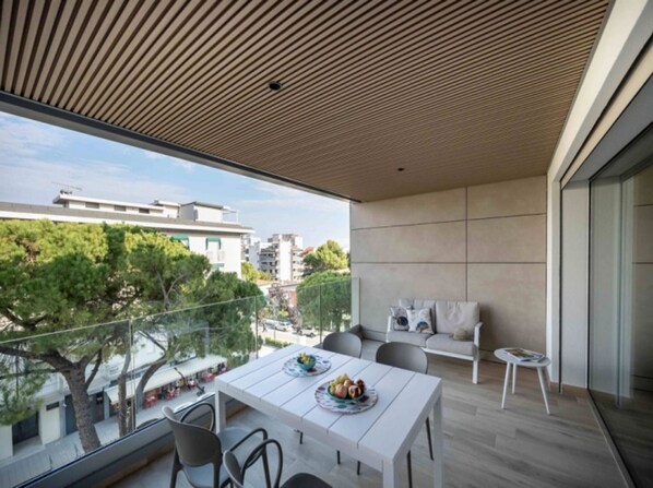 A modern balcony with a wooden ceiling, a dining table with chairs, and a sofa.
