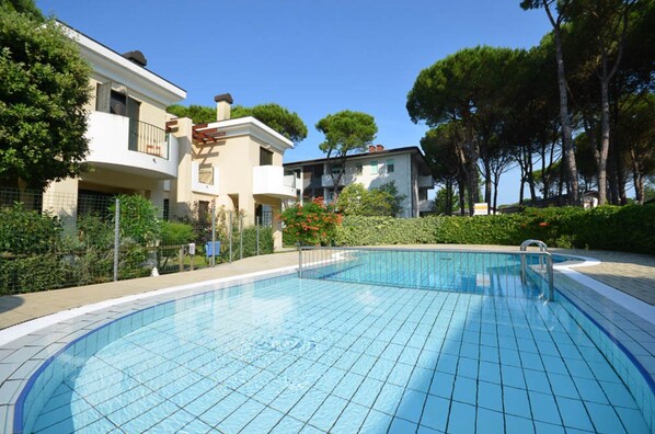 A swimming pool with tiled edges, surrounded by a fence and greenery.