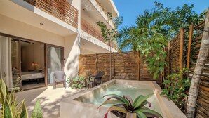 Zona de piscina exterior moderna amb una banyera d'hidromassatge, envoltada per una tanca de fusta i vegetació exuberant.