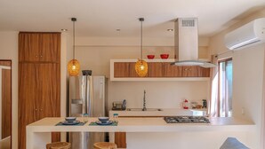 Una cuina moderna amb armaris de fusta, un frigorífic d'acer inoxidable, una illa central amb tamborets, llums penjants i una placa de cocció integrada.