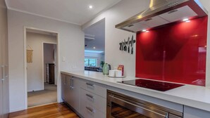 Uma cozinha moderna com exaustor de aço inoxidável, painel de fundo vermelho e lava-louças embutida.