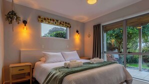 Quarto com cama grande, mesas de cabeceira, janela com cortinas e vista para o verde lá fora.