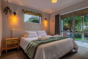A bedroom with a large bed, bedside tables, a window with curtains, and a view of greenery outside.