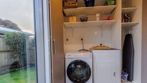 Uma lavanderia compacta com máquina de lavar frontal, secadora e uma prateleira com diversos objetos.