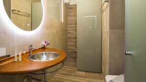 A modern bathroom with a wooden vanity, a round mirror, and a glass shower enclosure.