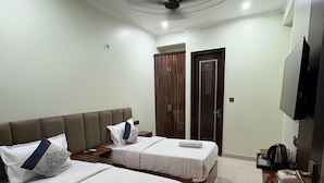 A hotel room with two beds, a ceiling fan, a wardrobe, a television, and a small table with a kettle. - Radiant Blu Hotels Sector 70 (Noida)