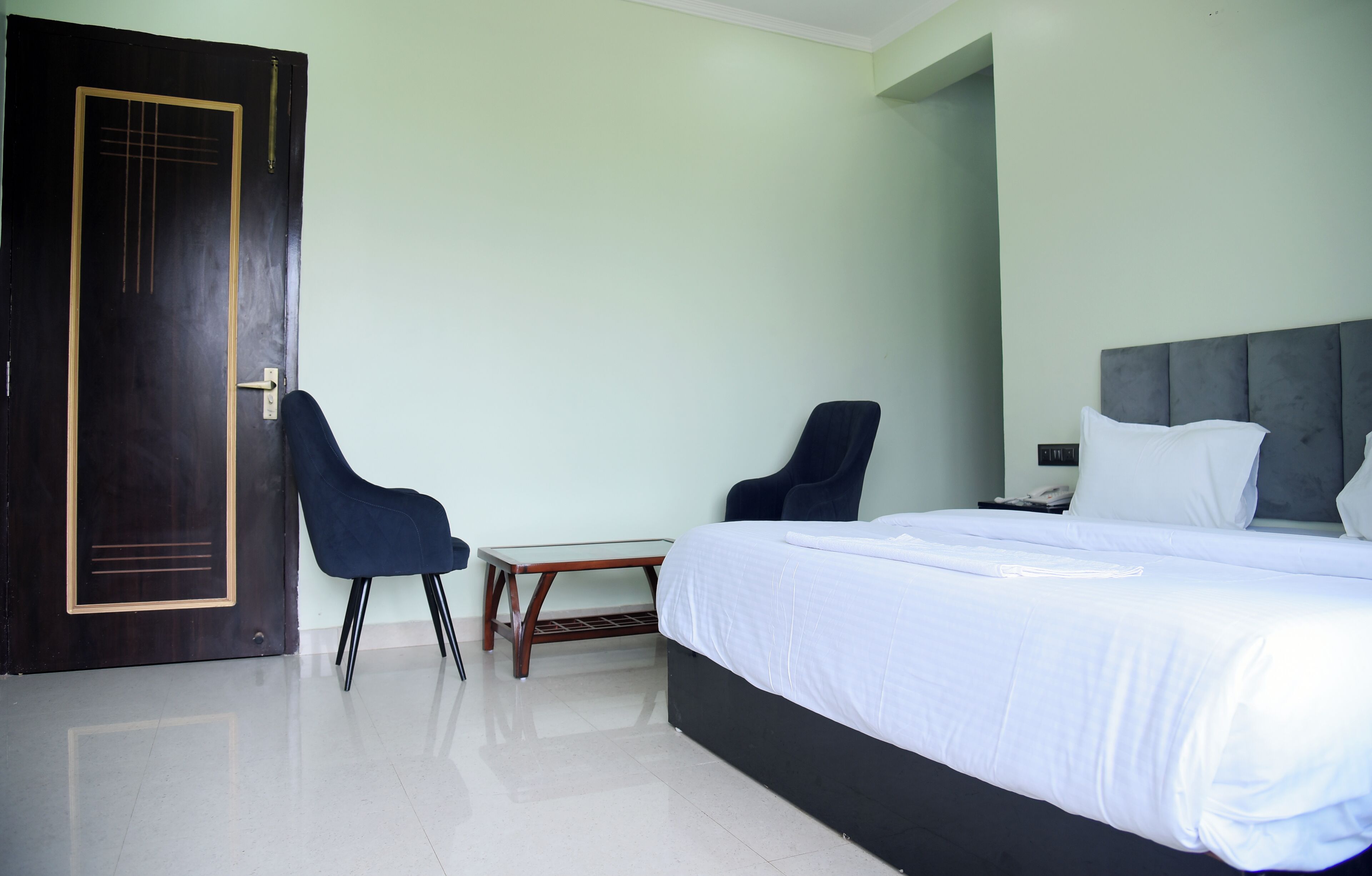 A hotel room with a large bed, two chairs, a small table, and a door.