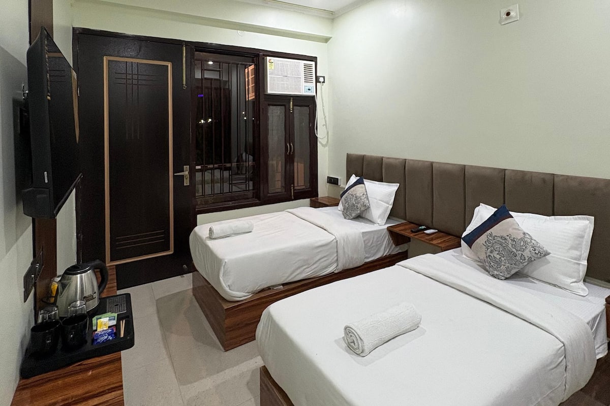 A hotel room with two single beds, a television, a wardrobe, and a ceiling fan.