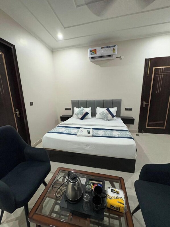 A hotel room with a bed, two chairs, a coffee table with a kettle, cups, and a snack package. - Radiant Blu Hotels Sector 70 (Noida)