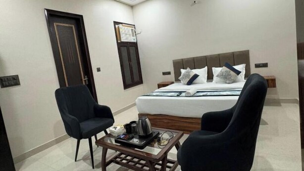 A hotel room with a bed, two chairs, a coffee table, a ceiling fan, and a door. - Radiant Blu Hotels Sector 70 (Noida)