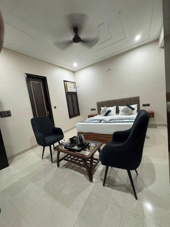 A hotel room with a bed, two chairs, a coffee table, a ceiling fan, and a door.