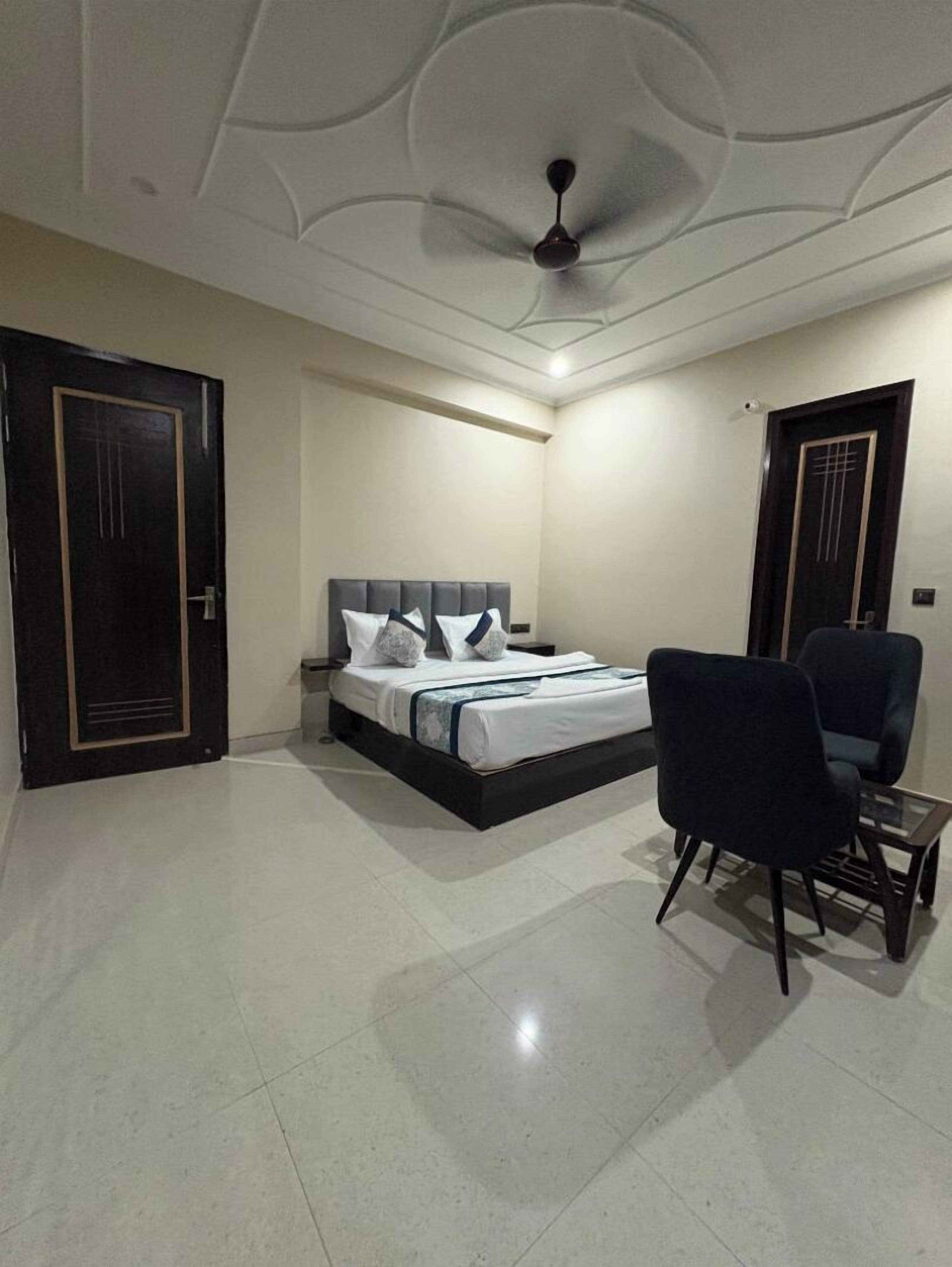 A bedroom with a bed, two chairs, a ceiling fan, and a door.