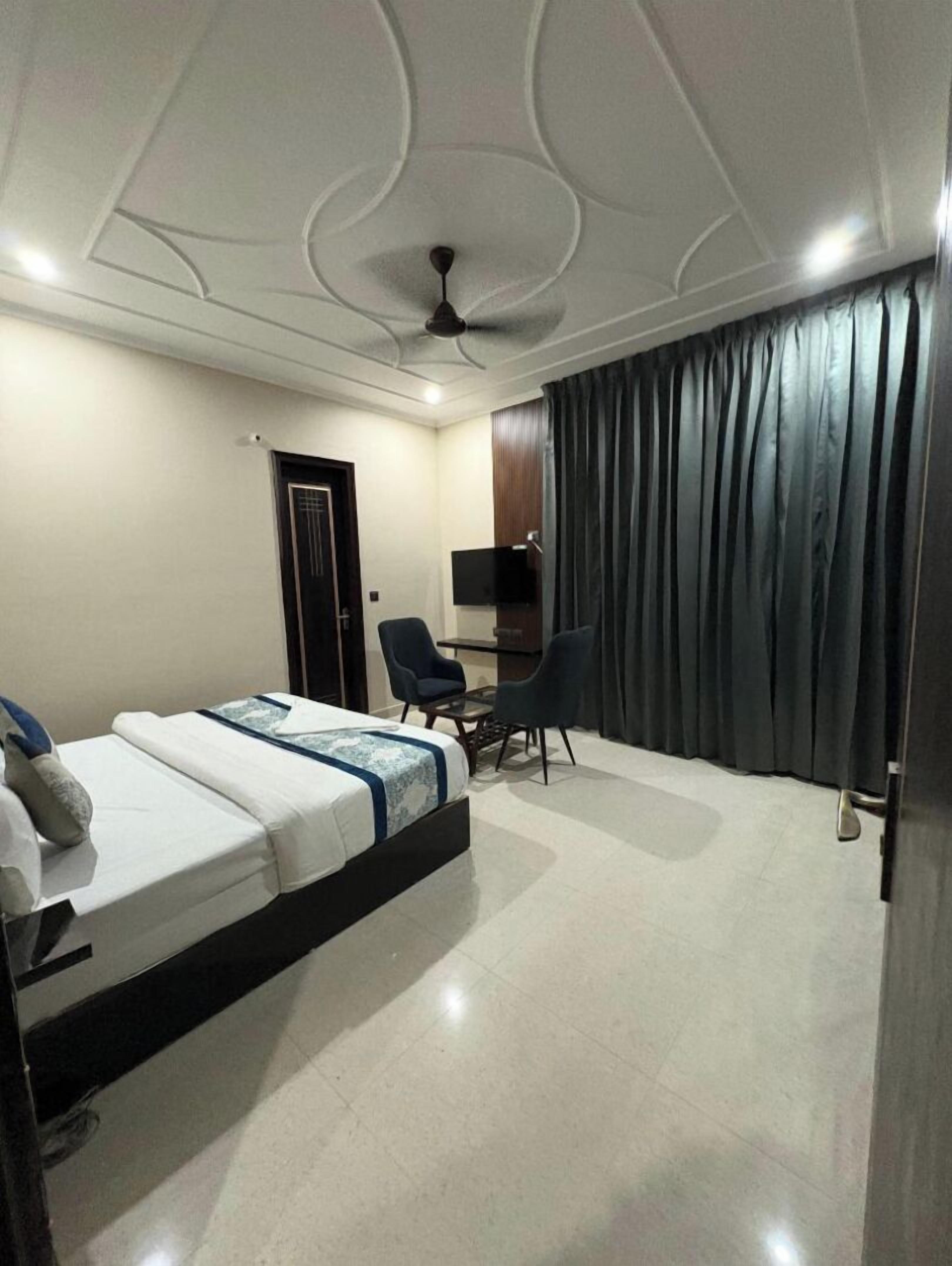 Una habitación de hotel con una cama, un escritorio, dos sillas, un ventilador de techo y un televisor.