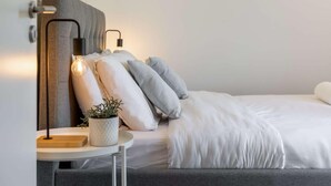 A neatly arranged bedroom with a bed, pillows, a bedside table with a lamp, and a small potted plant.