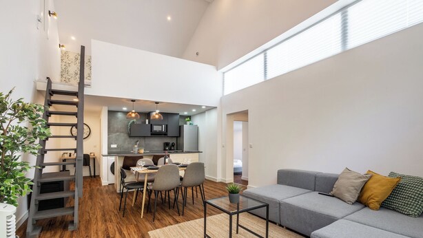 A modern living space with a dining area, kitchen, and a grey sofa with pillows.