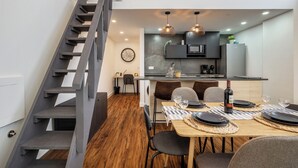 A modern kitchen with a dining area, a staircase, and a clock on the wall.