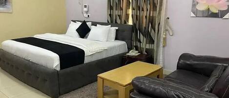A bedroom with a bed, a nightstand, a table, a sofa, a fan, and curtains.