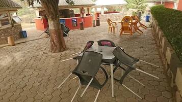 An outdoor seating area with hexagonal tile flooring, a table with chairs, and a kiosk in the background.