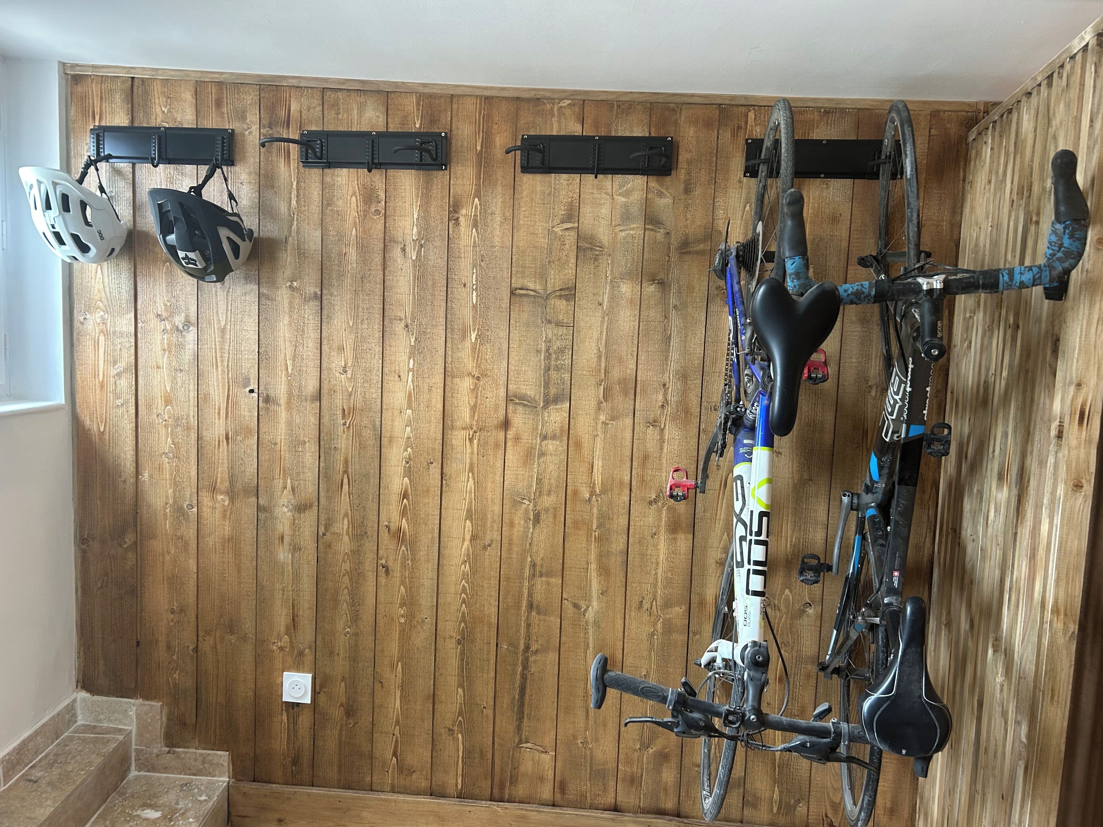 Een houten muur met een fietsenrek met twee helmen en een fiets.