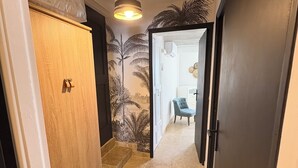 A hallway with a wooden wardrobe, a tiled floor, and a wall with a palm tree mural. - Charming village house with sauna (Bédoin)