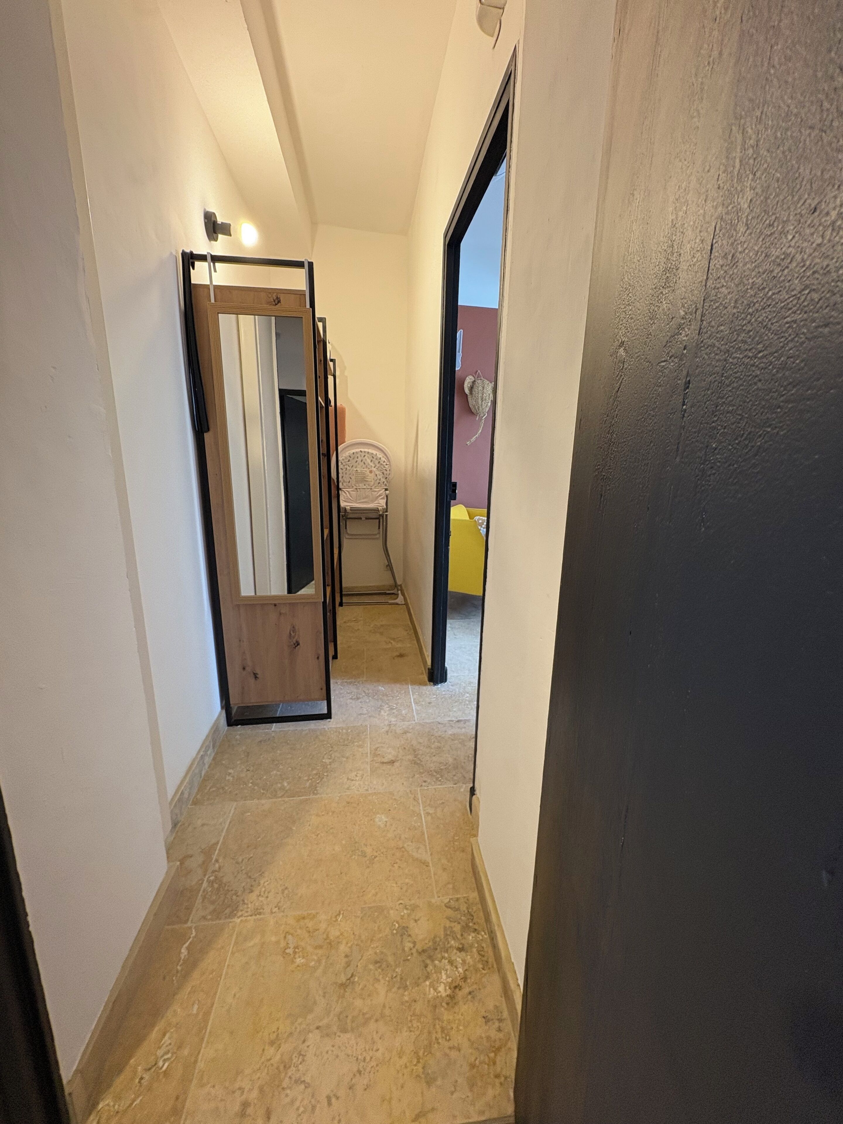 A narrow hallway with a tiled floor, a wooden door frame, and a chair.