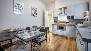 A modern kitchen with a dining area, featuring a kitchen island, built-in oven, and a coffee machine.