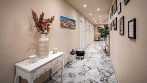 A hallway with a marble floor, a white console table with decorative items, and framed pictures on the walls.