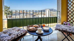 A balcony with a table set for breakfast, including pastries, a cup of coffee, and a glass of orange juice.