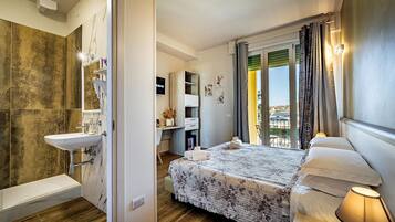 A modern hotel room with a large bed, a bedside table with a lamp, a bathroom with a sink and a hairdryer, and a view of the city through the window.