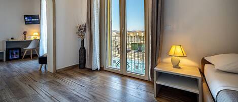 Une chambre d’hôtel avec un plancher en bois, un lit, un bureau avec une chaise, une télévision et un balcon avec vue.
