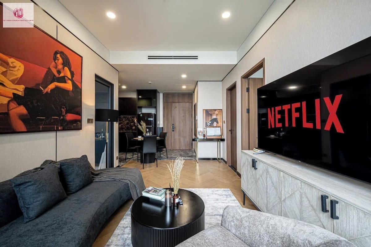 Un salon moderne avec un grand téléviseur à écran plat affichant le logo de Netflix, un canapé, une table basse et un tableau accroché au mur.