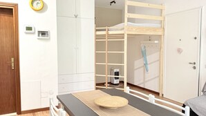 Um quarto com uma cama beliche, uma escrivaninha com cadeira, um guarda-roupa, um relógio e um aquecedor.