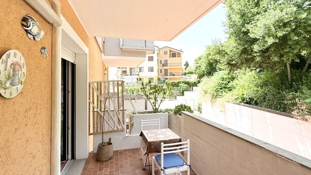Varanda com mesa e cadeiras, um relógio e vista para edifícios vizinhos e áreas verdes.