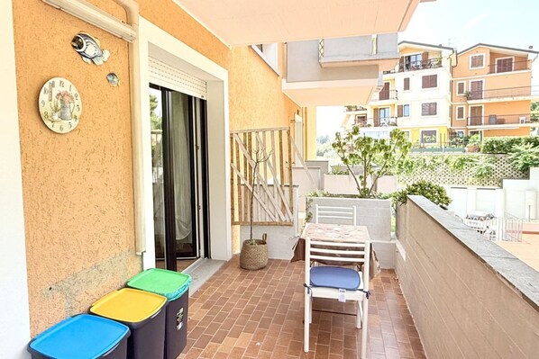 A balcony with a table and chairs, a trash bin, and a door.