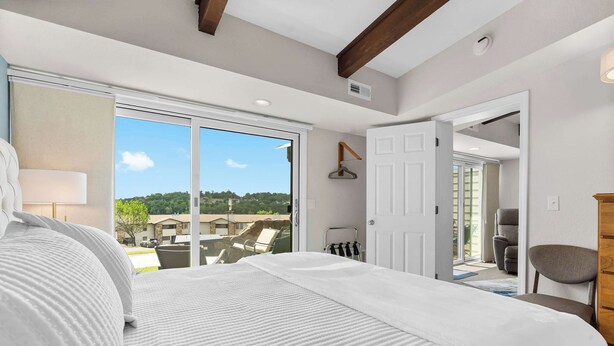 A bedroom with a large bed, a view of the outdoors, and a door leading to another room. - Little Dipper Cozy Condo for 6 w/ Resort-style Amenities (Kimberling City)