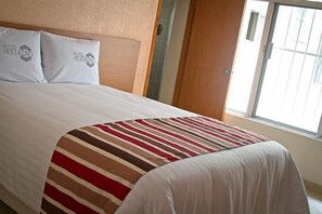 A hotel room with a bed, two pillows with 'HOTEL ESTADIO' text, a striped blanket, and a window with blinds. - Hotel del Estadio (Banderilla)
