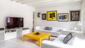 A modern living room with a flat-screen TV, white sofas, a yellow coffee table, and artwork on the walls. - Trieste - Spiridione (Trieste)