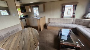 A compact RV interior with a kitchenette, a sofa, a dining table, and a glass coffee table. - Petfriendly- Familyfriendly- 8berth- Tattershall (Lincoln)