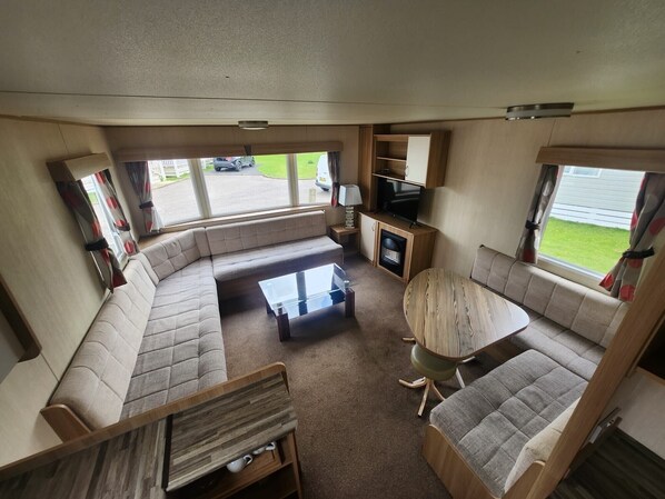 Interior de una caravana compacta con sofá, una mesita de centro, televisor y una pequeña cocina.