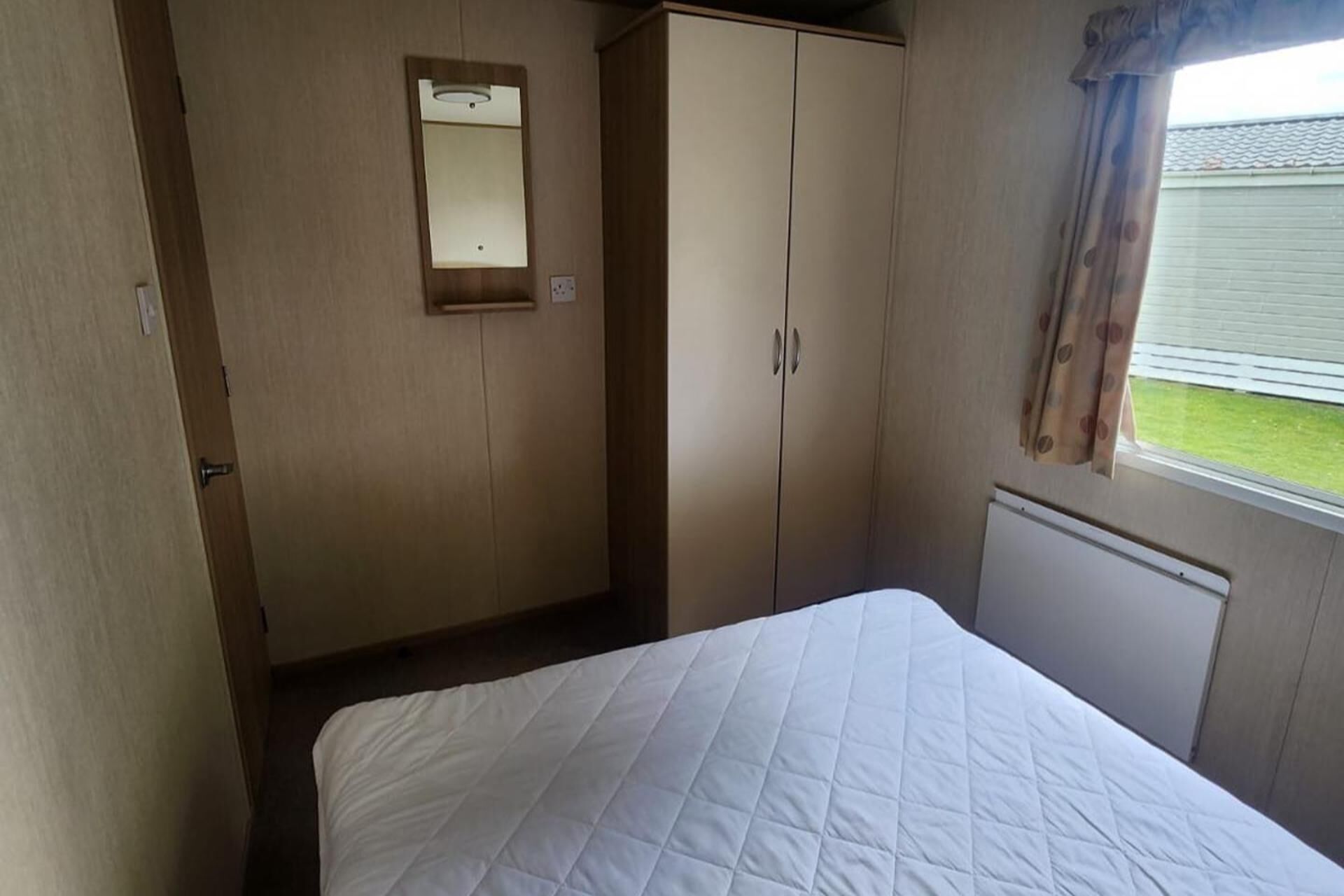 A bedroom with a bed, a wardrobe, a mirror, and a window with curtains.